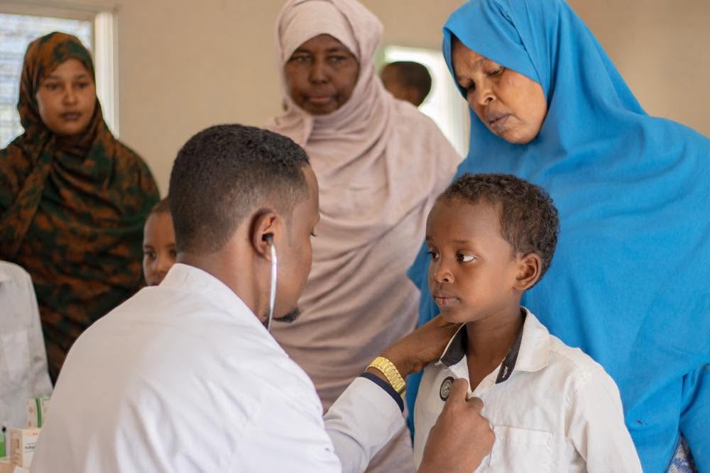 A doctor examining a young patient with a stethoscope while family members look on