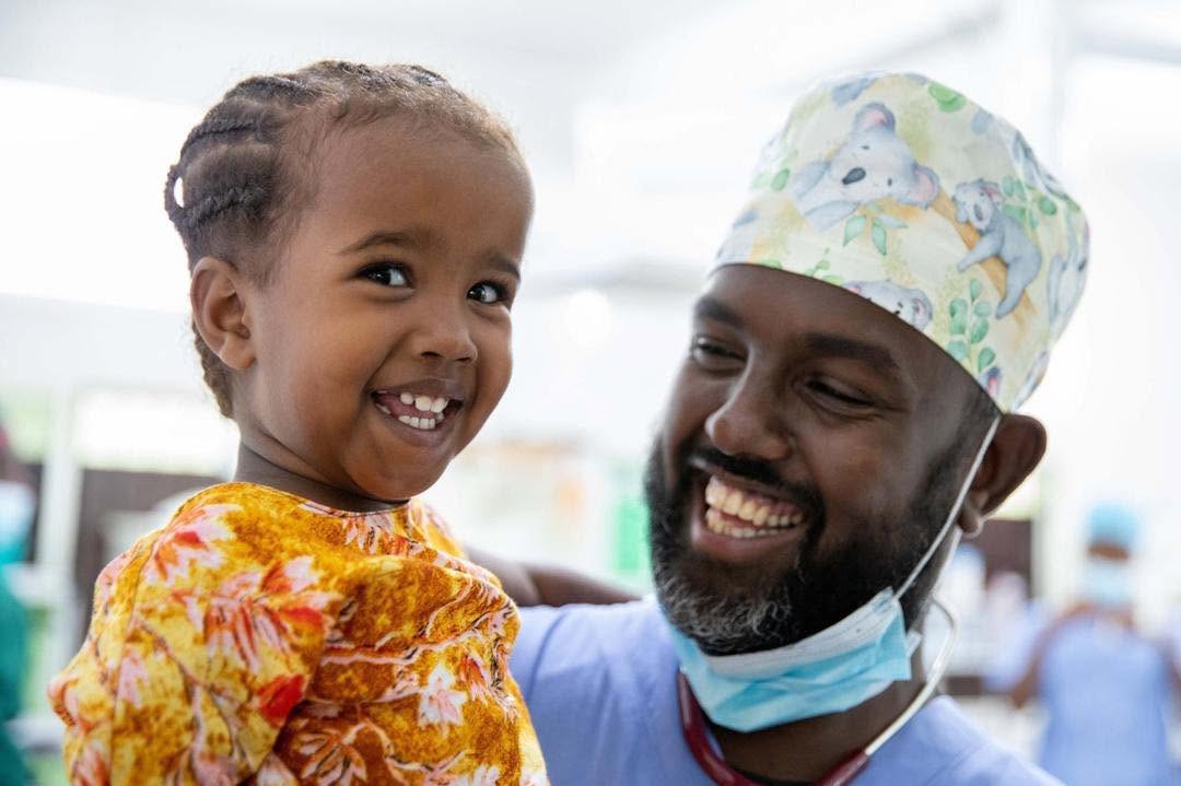 A hospital staff member holding and smiling with a young patient